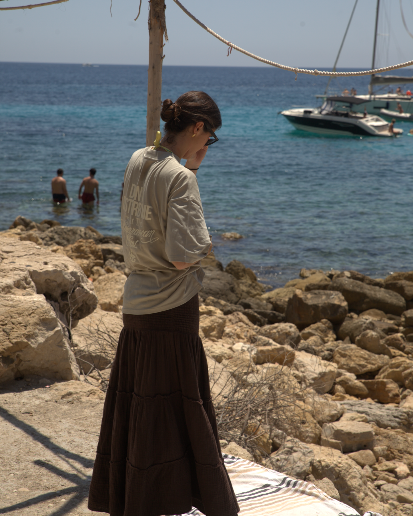Mujer junto al mar en una cala rocosa con camiseta oversize verde salvia de SQUALO